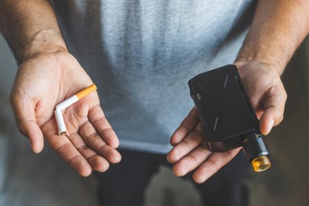 20220929_vape-vs-cig person holding a broken cigarette in one hand and a vape device in the other