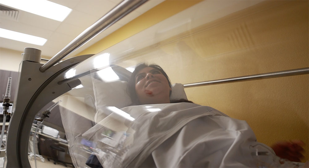 1000x544_CCMC_WoundCenter-06 A young Latina woman smiles as she rests in a hyperbaric oxygen chamber