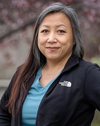 Nou Hou, RN, stands in front of a field of blossoming trees