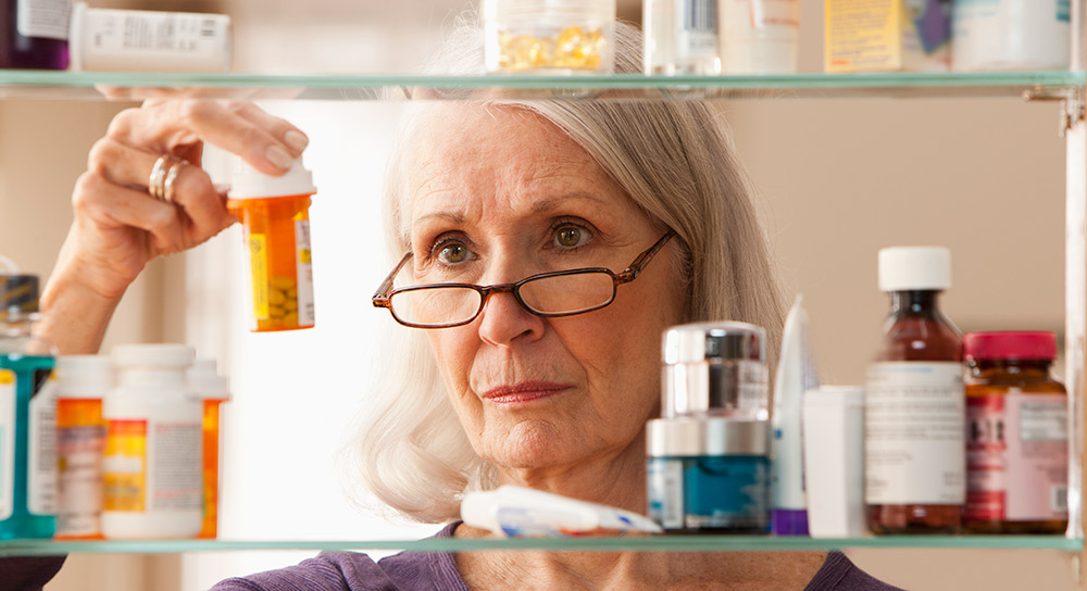 A pharmacist, older and white female, looks closely at a pill bottle.