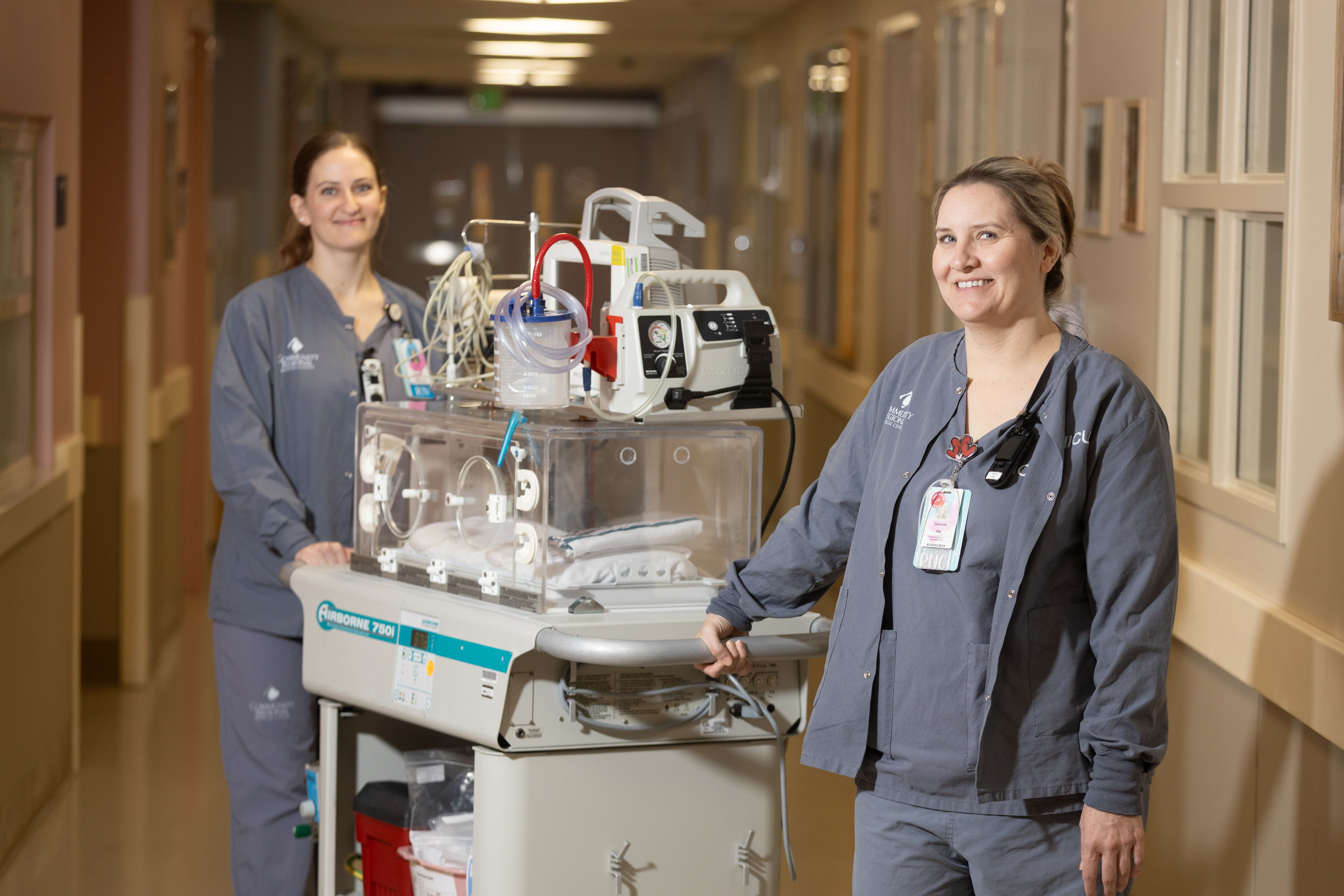 Two nurses stand on either side of an empty NICU ventilator