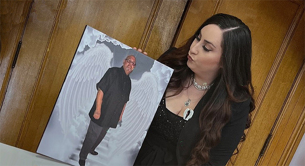 Savannah Dominguez holds up a large image of her father standing in front of angel wings.