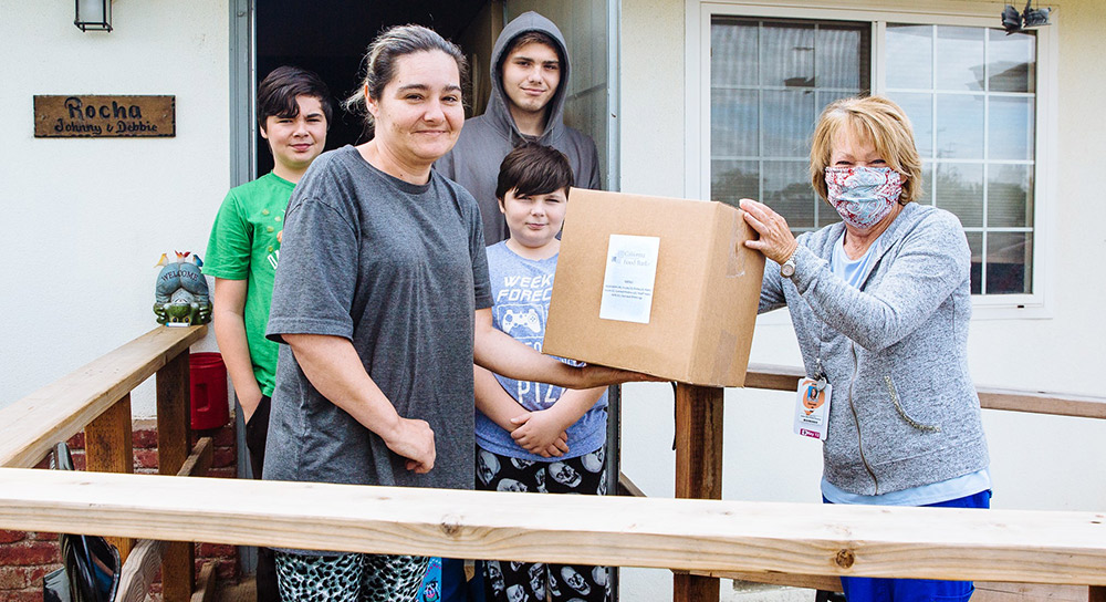 A young family receives a box of food from a woman in a mask