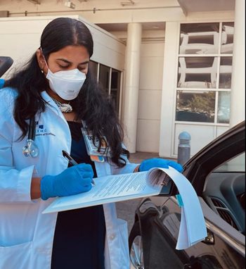 Dr. Geetha Sivasubramanian wears a mask and checks a patient's records on a clipboard