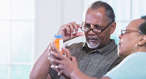 An older couple, man and woman, both Black, read the label on a prescription drug bottle.