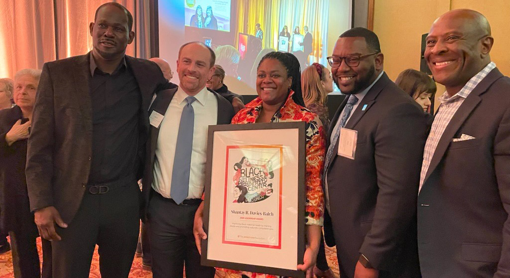 Shantay Davies-Balch stands in the middle of a group holding her framed award