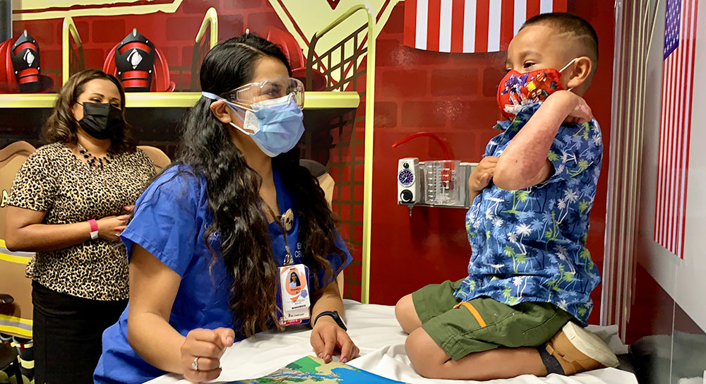 A mom looks on as her child is tended to by a child life specialist